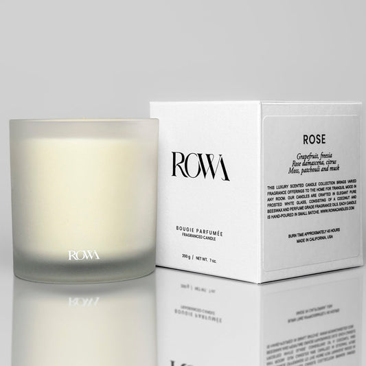 ROWA Rose candle in a frosted glass jar, surrounded by soft petals and greenery, styled to evoke a rainy day rose garden atmosphere.