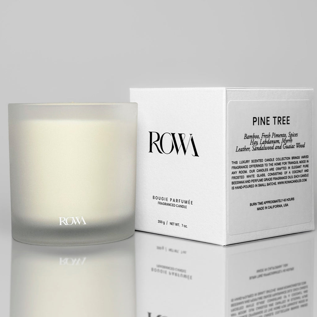 ROWA Pine Tree candle in frosted glass, styled with greenery and dark wood to evoke a grounding forest atmosphere with bamboo and leather notes.
